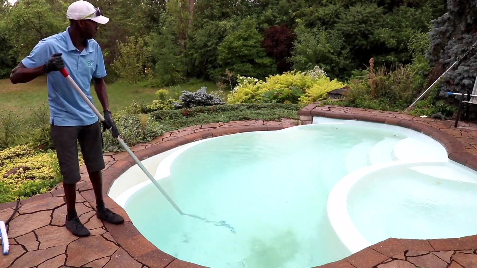 Technicien d'Entretien PCS qui passe l'aspirateur au fond d'une piscine creusée à l'eau turquoise
